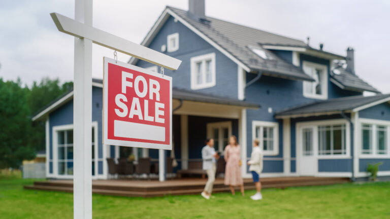 Red 'FOR SALE' real estate yard sign in front of a house