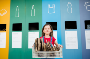 Girl recycling cardboard near bins.
