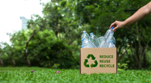 Hand placing bottle in box with a sign of reduce reuse and recycle.